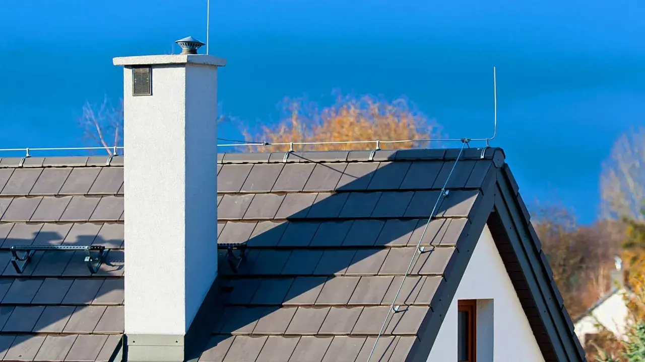Dach z szarej dachówki, biały komin i instalacja odgromowa. Czy instalacja odgromowa jest obowiązkowa? To pytanie zadaje sobie wielu właścicieli domów.