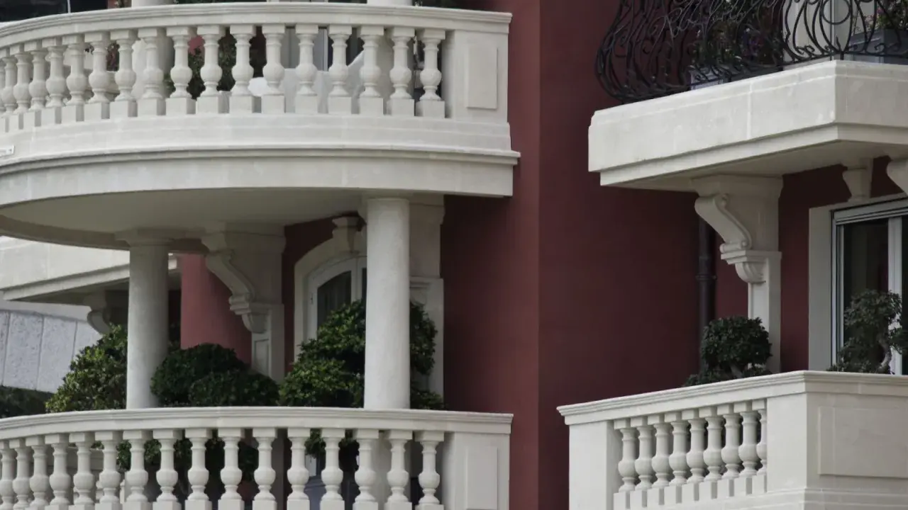 Eleganckie balustrady balkonowe z kamienia, z widocznym mocowaniem balustrady przez styropian, otaczają budynek o bordowej fasadzie.