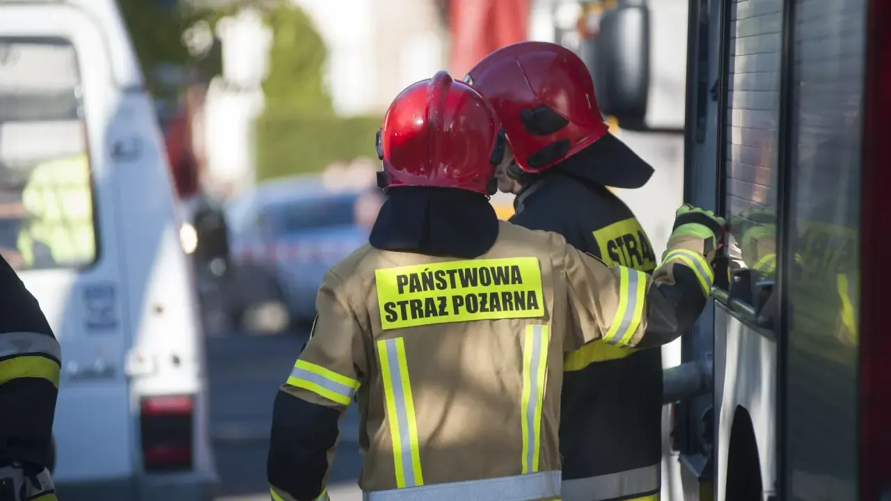 Strażacy w hełmach i mundurach Państwowej Straży Pożarnej przygotowują się do odbioru budynku.
