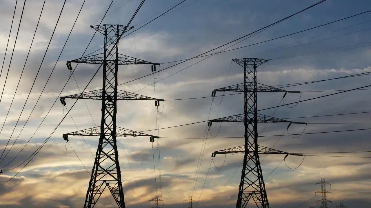 Dwa wysokie słupy energetyczne na tle zachodzącego słońca. Sieć przewodów tworzy skomplikowany wzór. Zastanawiasz się, ile to jeden kw?