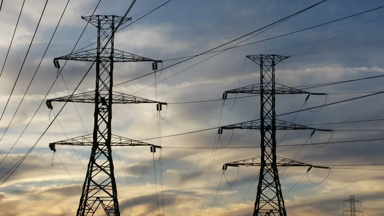 Dwa wysokie słupy energetyczne na tle zachodzącego słońca. Zastanawiasz się, ile za kilowat prądu?