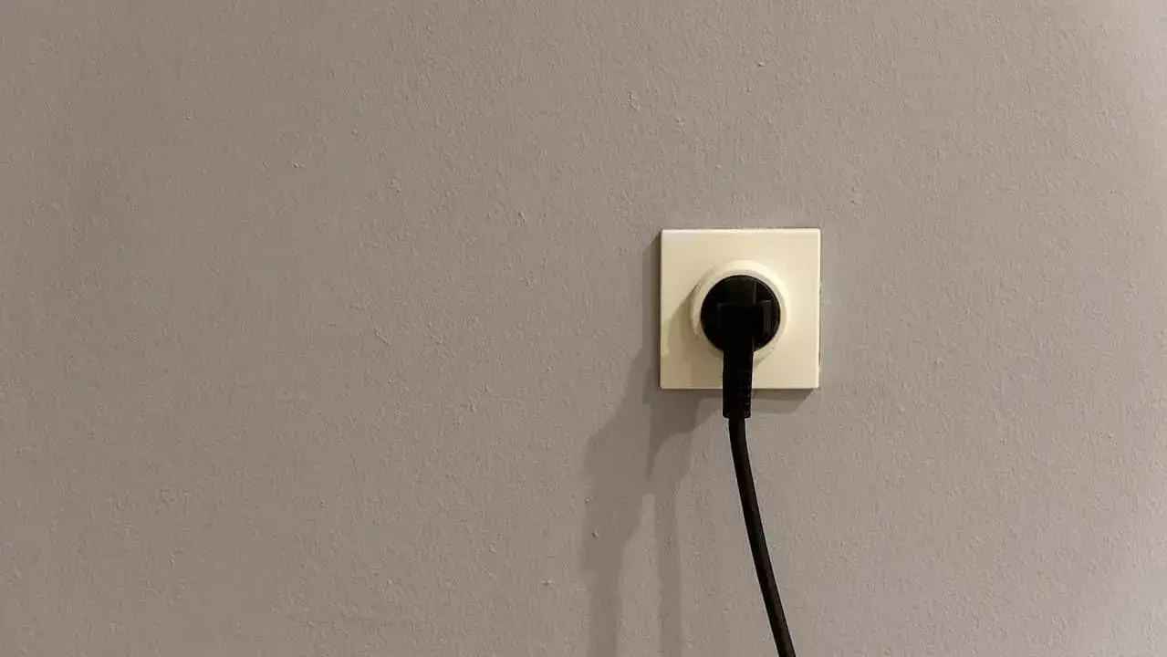 Gniazdko elektryczne z wtyczką. Szara ściana, symbol oszczędności i tani prąd.