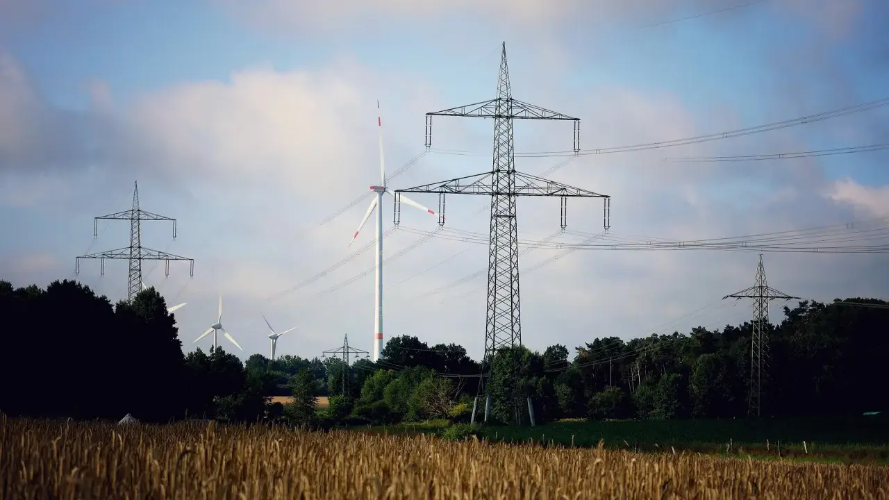Pole pszenicy, wiatraki i wysokie słupy energetyczne tworzą krajobraz nowoczesnej sieci OSD.