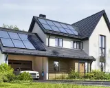 Nowoczesny dom z panelami fotowoltaicznymi na dachu. Obok stoi biały samochód z ładowarką. To właśnie oze co to – energia odnawialna w praktyce.
