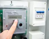 Palec wskazuje stan licznika energii elektrycznej: 00000000717.0 kWh. Obok widoczny wyłącznik.