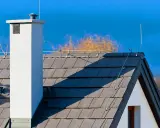 Dach z szarej dachówki, biały komin i instalacja odgromowa. Czy instalacja odgromowa jest obowiązkowa? To pytanie zadaje sobie wielu właścicieli domów.