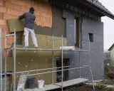 Budowlaniec montuje izolację na ścianie domu. Warstwa po warstwie, styropian na styropian, tworząc ciepłą powłokę.