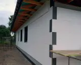 Budowa domu w toku. Ściany ocieplone grubym styropianem na placki, widoczne drewniane elementy dachu i okna.