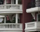 Eleganckie balustrady balkonowe z kamienia, z widocznym mocowaniem balustrady przez styropian, otaczają budynek o bordowej fasadzie.
