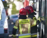 Strażacy w hełmach i mundurach Państwowej Straży Pożarnej przygotowują się do odbioru budynku.