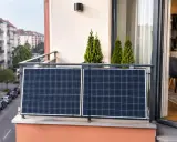 Dwa panele fotowoltaiczne na balkonie, widok na ulicę i kamienice. Montaż paneli bez zgody wspólnoty może budzić kontrowersje.