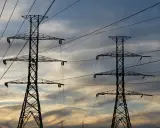 Dwa wysokie słupy energetyczne na tle zachodzącego słońca. Sieć przewodów tworzy skomplikowany wzór. Zastanawiasz się, ile to jeden kw?