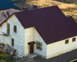 Nowy dom w zabudowie siedliskowej, z ciemnobordowym dachem i białymi ścianami, czeka na wykończenie.