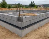 Fundament domu w trakcie budowy. Murowanie z bloczka betonowego, widoczne zbrojenie i poziomica.