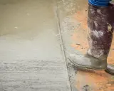 Pracownik w gumowcach stoi na świeżym betonie. Widać mokry cement z wodą bez piasku, tworzący gładką powierzchnię.