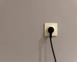 Gniazdko elektryczne z wtyczką. Szara ściana, symbol oszczędności i tani prąd.