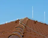 System piorunochronu na brązowym dachu z dachówki ceramicznej, chroniący przed uderzeniami pioruna.