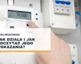 Opis licznika dwukierunkowego. Dłoń wskazuje na ekran licznika energii elektrycznej, pokazując jego odczyty.