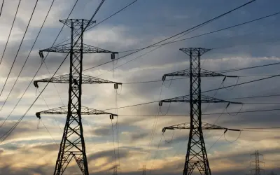 Dwa wysokie słupy energetyczne na tle zachodzącego słońca. Zastanawiasz się, ile za kilowat prądu?