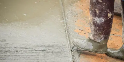 Pracownik w gumowcach stoi na świeżym betonie. Widać mokry cement z wodą bez piasku, tworzący gładką powierzchnię.