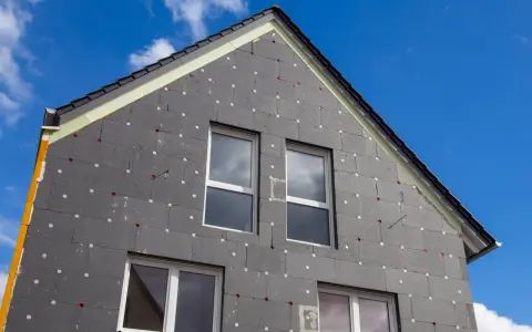 Izolacja domu z grafitowego styropianu, z widocznymi oknami i dachem. Czy styropian się pali? To pytanie nurtuje wielu, ale nowoczesne materiały są bezpieczne.