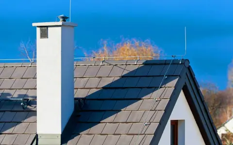 Dach z szarej dachówki, biały komin i instalacja odgromowa. Czy instalacja odgromowa jest obowiązkowa? To pytanie zadaje sobie wielu właścicieli domów.