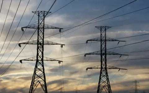 Dwa wysokie słupy energetyczne na tle zachodzącego słońca. Sieć przewodów tworzy skomplikowany wzór. Zastanawiasz się, ile to jeden kw?