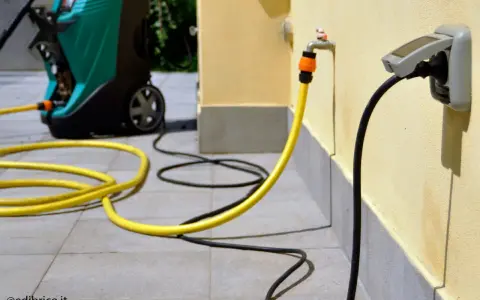 Jak zamontować gniazdko na elewacji? Wąż ogrodowy podłączony do kranu i kabel zasilający do gniazdka na ścianie.