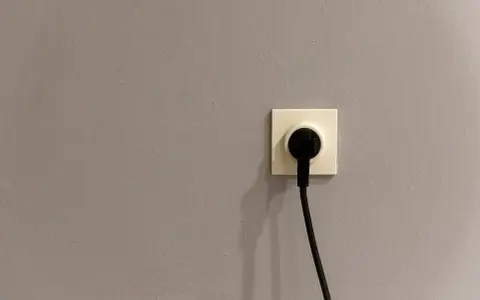 Gniazdko elektryczne z wtyczką. Szara ściana, symbol oszczędności i tani prąd.