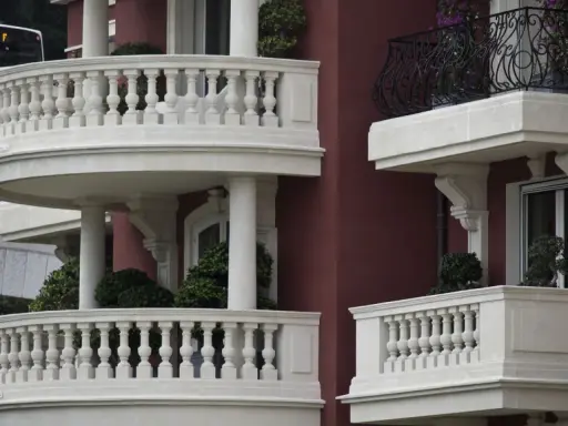 Eleganckie balustrady balkonowe z kamienia, z widocznym mocowaniem balustrady przez styropian, otaczają budynek o bordowej fasadzie.