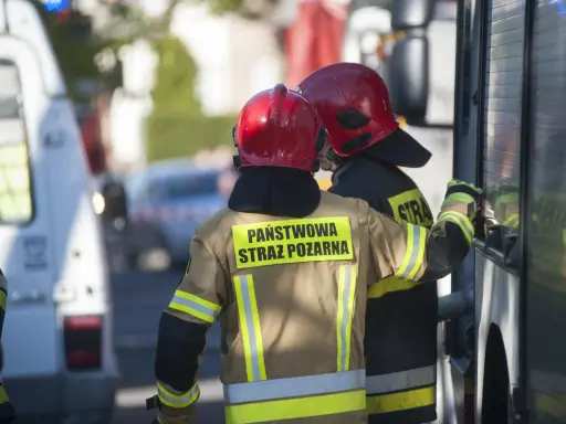 Strażacy w hełmach i mundurach Państwowej Straży Pożarnej przygotowują się do odbioru budynku.