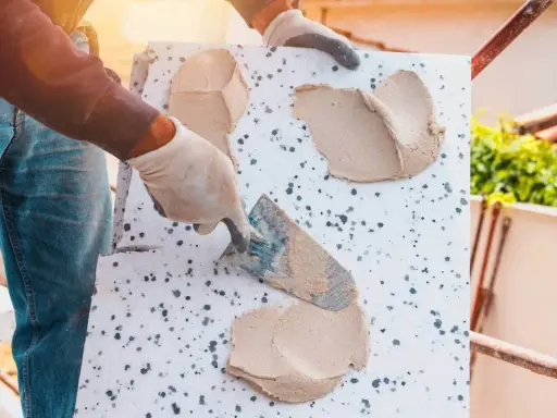 Ręce w rękawiczkach nakładają zaprawę na styropian, przygotowując go do układania płytek elewacyjnych.