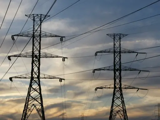 Dwa wysokie słupy energetyczne na tle zachodzącego słońca. Sieć przewodów tworzy skomplikowany wzór. Zastanawiasz się, ile to jeden kw?