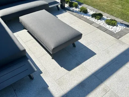 Nowoczesny taras z szarymi meblami, gdzie trwa układanie płyt tarasowych na podsypce. W tle rabata z białymi kamieniami i bukszpanami.