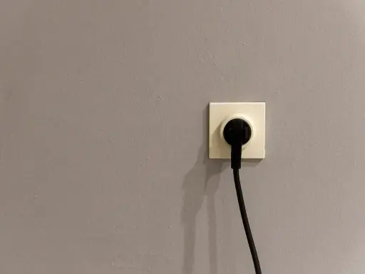 Gniazdko elektryczne z wtyczką. Szara ściana, symbol oszczędności i tani prąd.