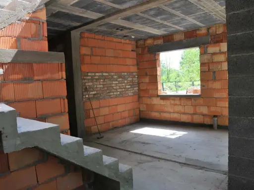Trwa przekształcenie budynku gospodarczego na mieszkalny. Widoczne schody, ściany z pustaków ceramicznych i betonowy strop.