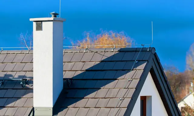 Dach z szarej dachówki, biały komin i instalacja odgromowa. Czy instalacja odgromowa jest obowiązkowa? To pytanie zadaje sobie wielu właścicieli domów.