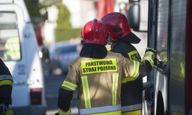 Strażacy w hełmach i mundurach Państwowej Straży Pożarnej przygotowują się do odbioru budynku.