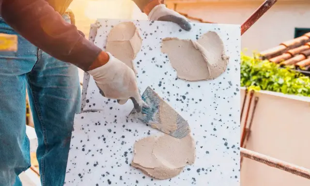 Ręce w rękawiczkach nakładają zaprawę na styropian, przygotowując go do układania płytek elewacyjnych.