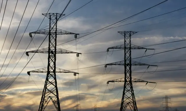Dwa wysokie słupy energetyczne na tle zachodzącego słońca. Sieć przewodów tworzy skomplikowany wzór. Zastanawiasz się, ile to jeden kw?