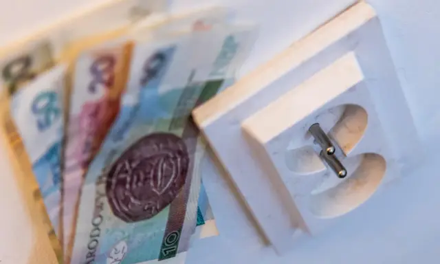 Polskie banknoty obok gniazdka elektrycznego, symbolizujące koszty energii. PGE okres rozliczeniowy G11.