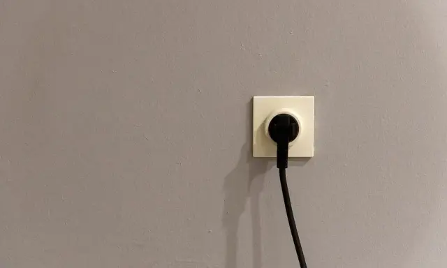 Gniazdko elektryczne z wtyczką. Szara ściana, symbol oszczędności i tani prąd.