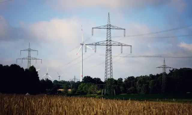 Pole pszenicy, wiatraki i wysokie słupy energetyczne tworzą krajobraz nowoczesnej sieci OSD.