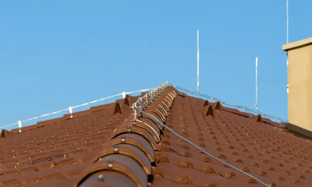 System piorunochronu na brązowym dachu z dachówki ceramicznej, chroniący przed uderzeniami pioruna.