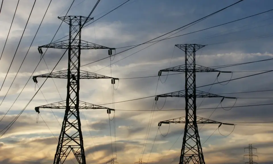 Dwa wysokie słupy energetyczne na tle zachodzącego słońca. Zastanawiasz się, ile za kilowat prądu?