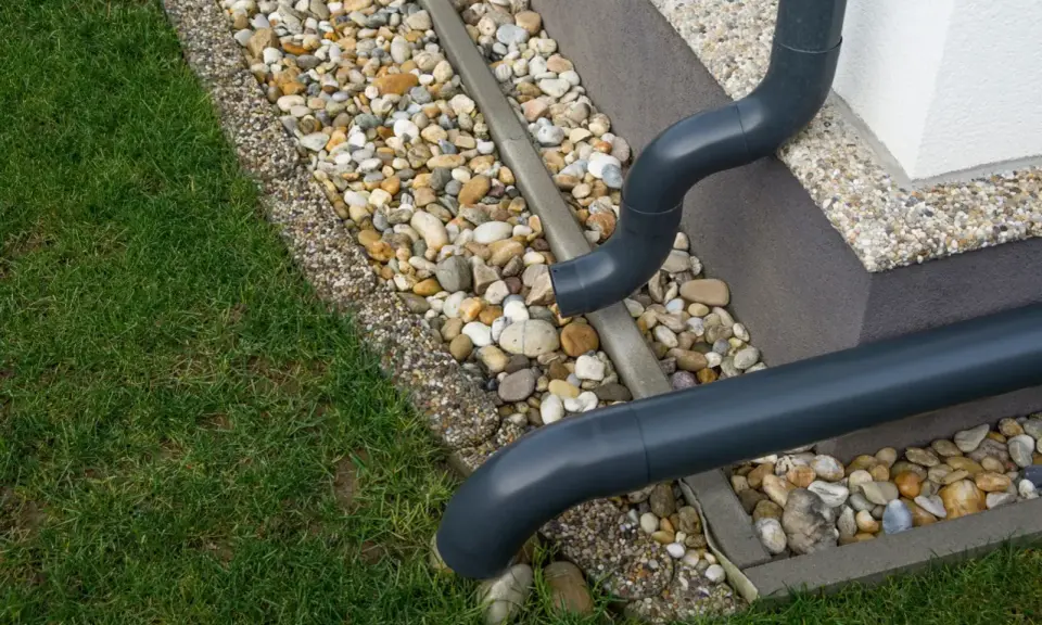 Domowe odprowadzenie wody deszczowej z rynien. Rury odprowadzają wodę na kamieniste podłoże przy trawniku.