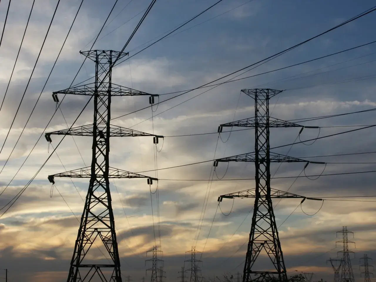 Dwa wysokie słupy energetyczne na tle zachodzącego słońca. Zastanawiasz się, ile za kilowat prądu?