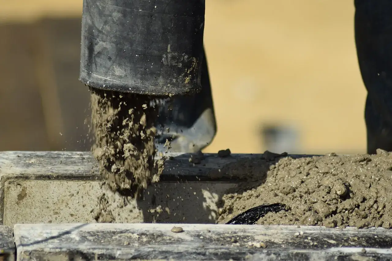 Beton z wodą bez piasku leje się z czarnej rury na budowie.