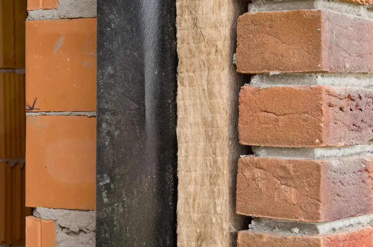 Warstwa izolacji z wełny mineralnej obok czarnej membrany i cegieł. Zastanawiasz się, ile to 10 cm styropianu ile to muru?