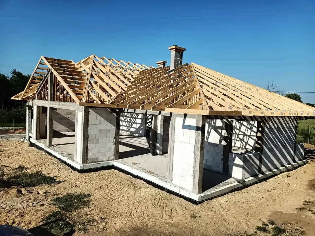 Budowa domu z betonowych pustak&oacute;w, widoczny drewniany dach bez murłaty, komin.